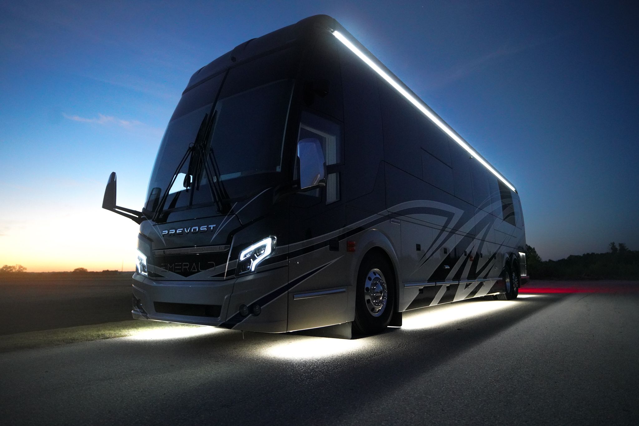 A silver and red luxury motorcoach parked in front of a blue night sky