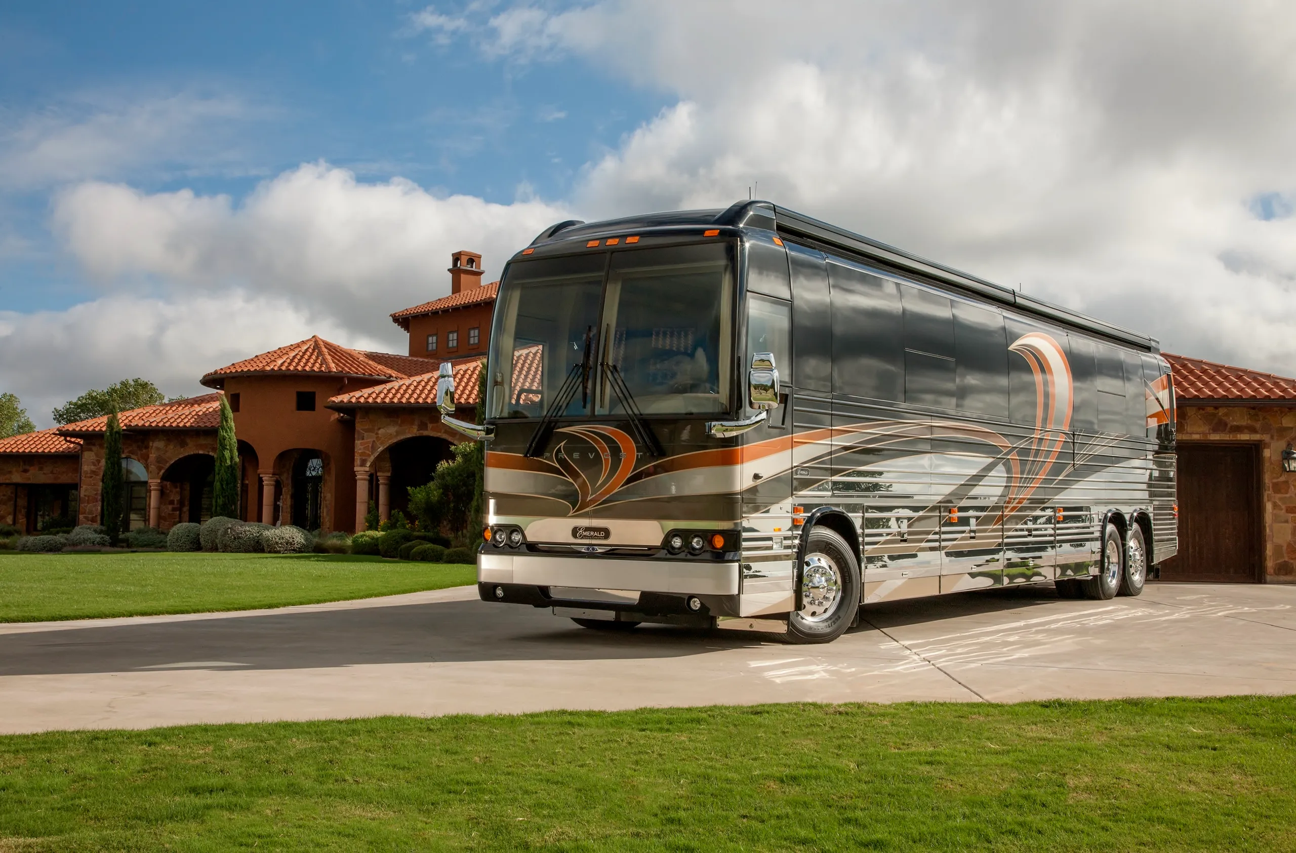 An orange and silver recreational vehicle in front of a rustic mansion