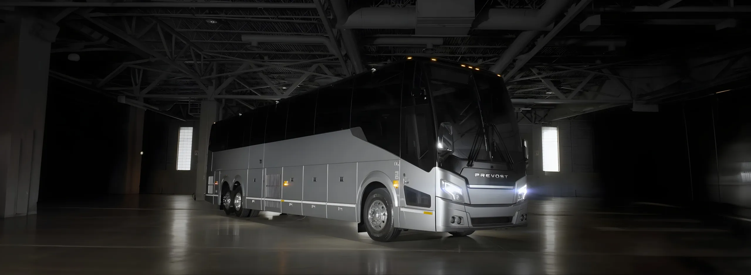 A silver and black motorcoach parked inside of a hangar